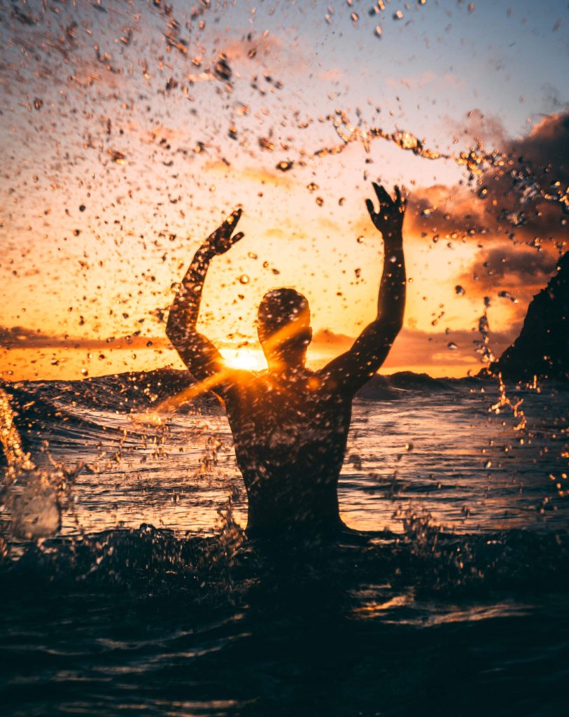 Person joyously splashing water into the air at sunset, symbolising the exhilaration of embracing life's journey with purpose and passion.