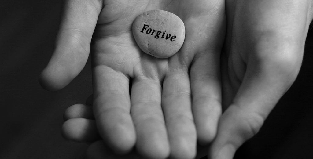 hand holding stone with the word forgive symbolising forgiveness, emotional healing, and letting go of past pain